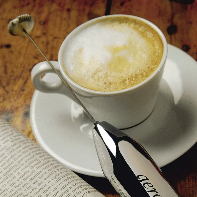 Aerolatte Foamer-Battery Powered sitting beside latte cup on wooden table.