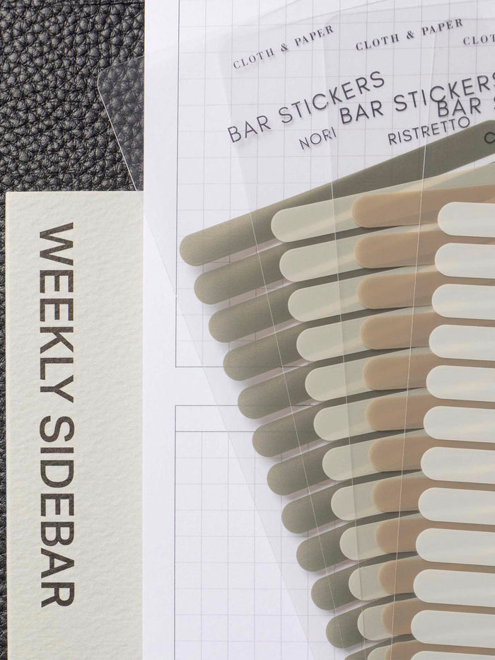 Set of four sticker sheets layered over each other inside a black leather planner. A Long Weekly Sidebar sticky note is visible beneath everything.