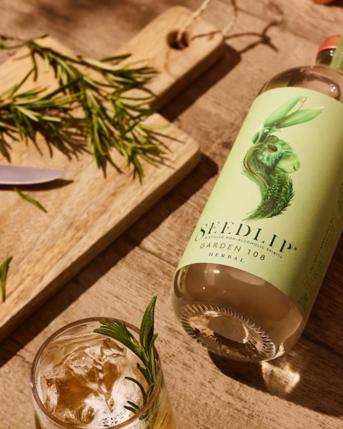 Bottle of Seedlip Garden 108 Herbal and glass on a wooden surface with herbs