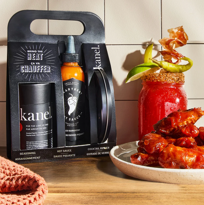 Kanel hot sauce packaging with a Bloody Mary and wings on a wooden surface.