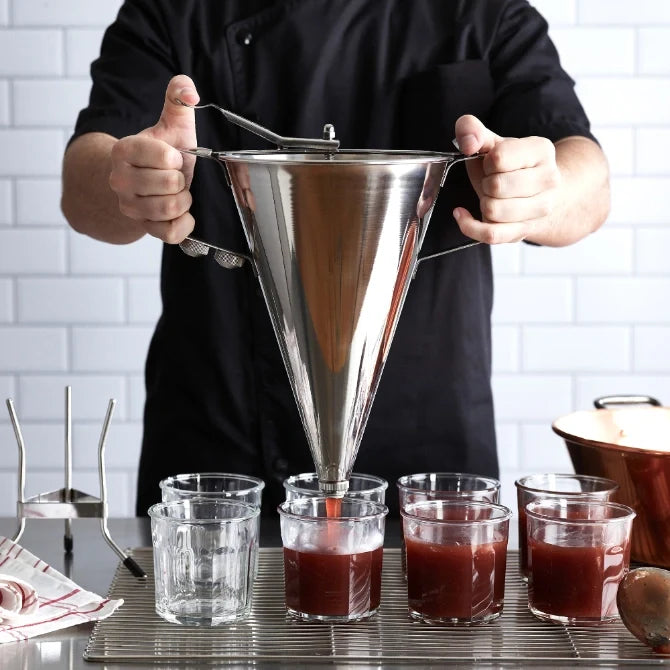 Stainless steel automatic funnel (sauce gun) with two handles and a lever for dispensing, showing chef dispensing red liquid into clear glasses.