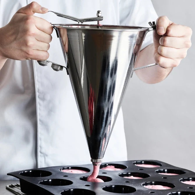 Stainless steel automatic funnel (sauce gun) with two handles and a lever for dispensing, showing chef dispensing pink liquids into black silicone mold.