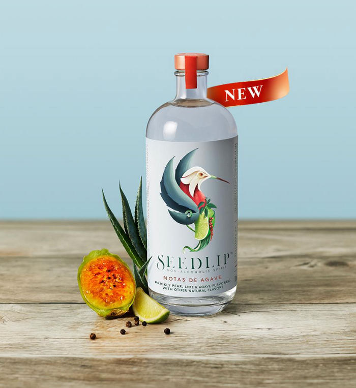 Seedlip Notas de Agave bottle with guava and lime on a wooden surface against a light blue background