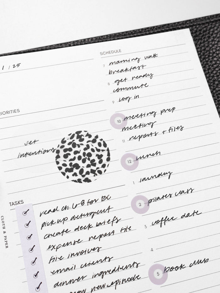 Closeup of inserts in use inside a leather planner. They are filled out with sample text and have been decorated with Spotlight stickers, Strips planner stickers, and a transparent Circle Page Flag.